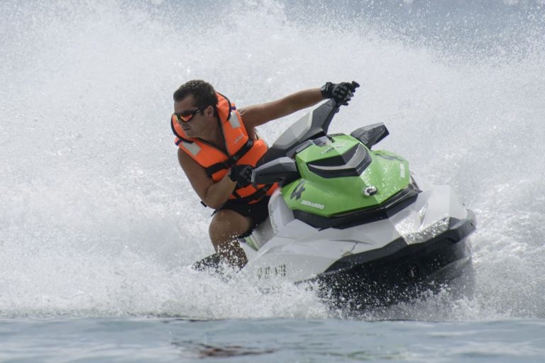 A person wearing an orange life jacket riding a green and white jet ski on water.