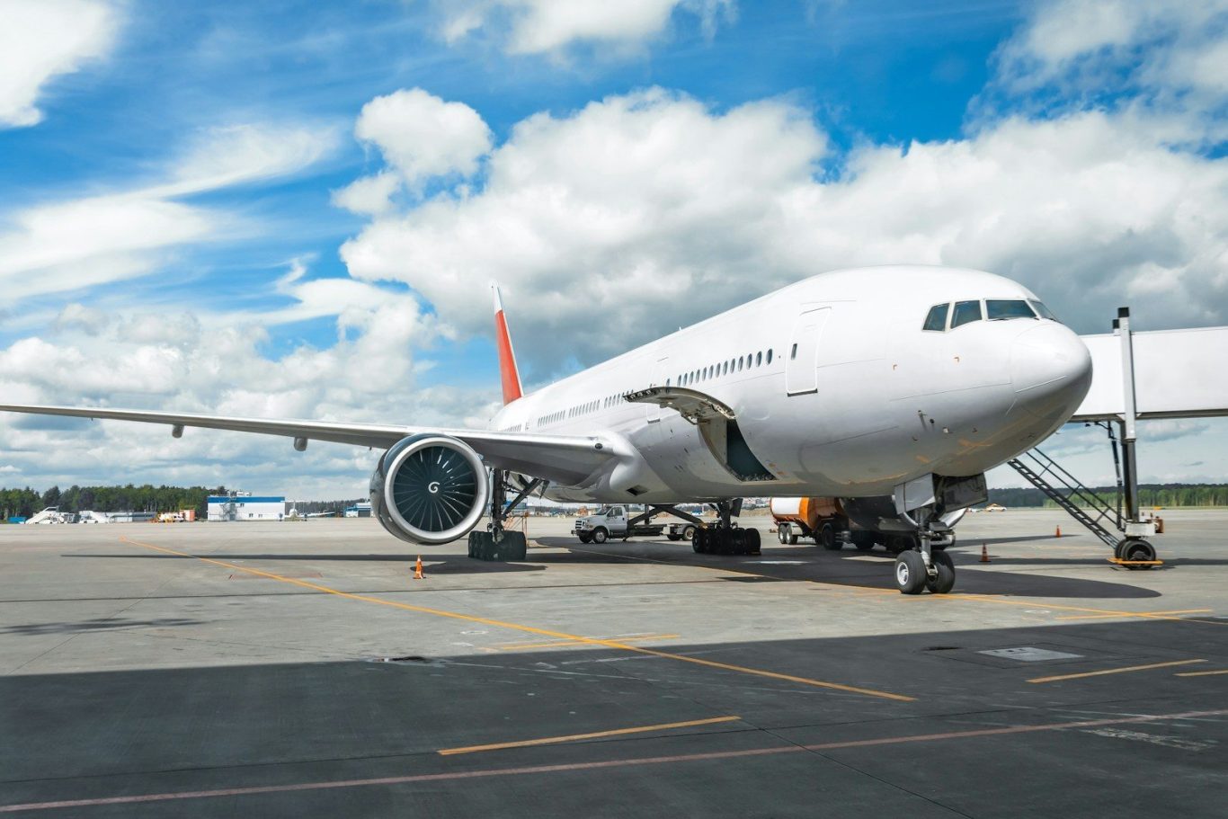 A white passenger jet on the tarmac under a partly cloudy sky.