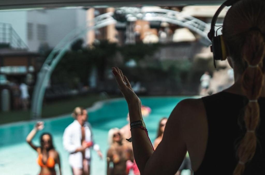 A DJ performing by a pool while guests enjoy the party atmosphere.