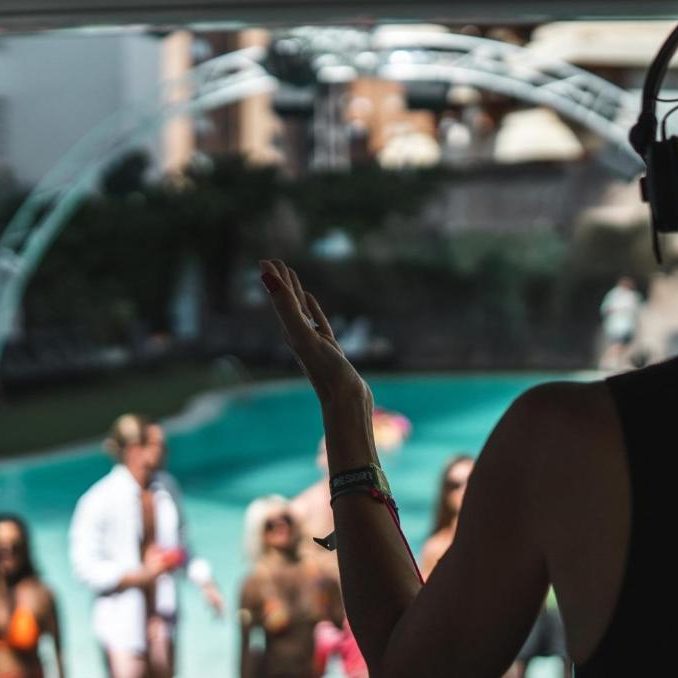 DJ mixes music at a lively pool party with attendees enjoying the atmosphere.