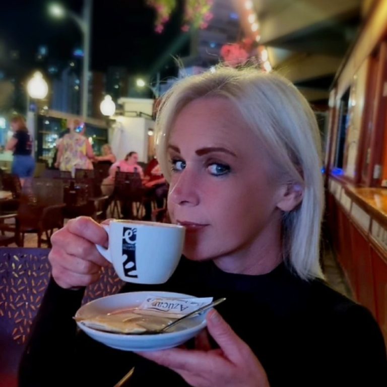 Woman in a café holding a cup of coffee and a plate of food, with city lights in the background.