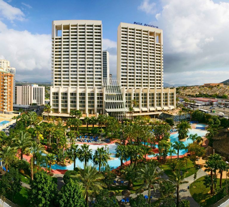 Meliá Benidorm Modern hotel towers overlook a landscaped pool area with palm trees and vibrant gardens.