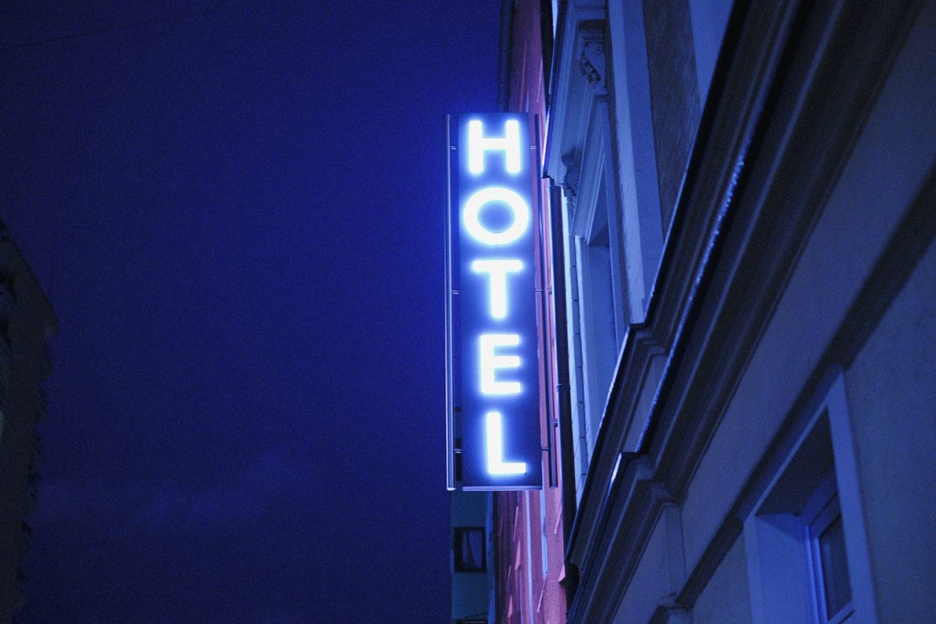 Neon blue "HOTEL" sign illuminated in a dark urban environment.
