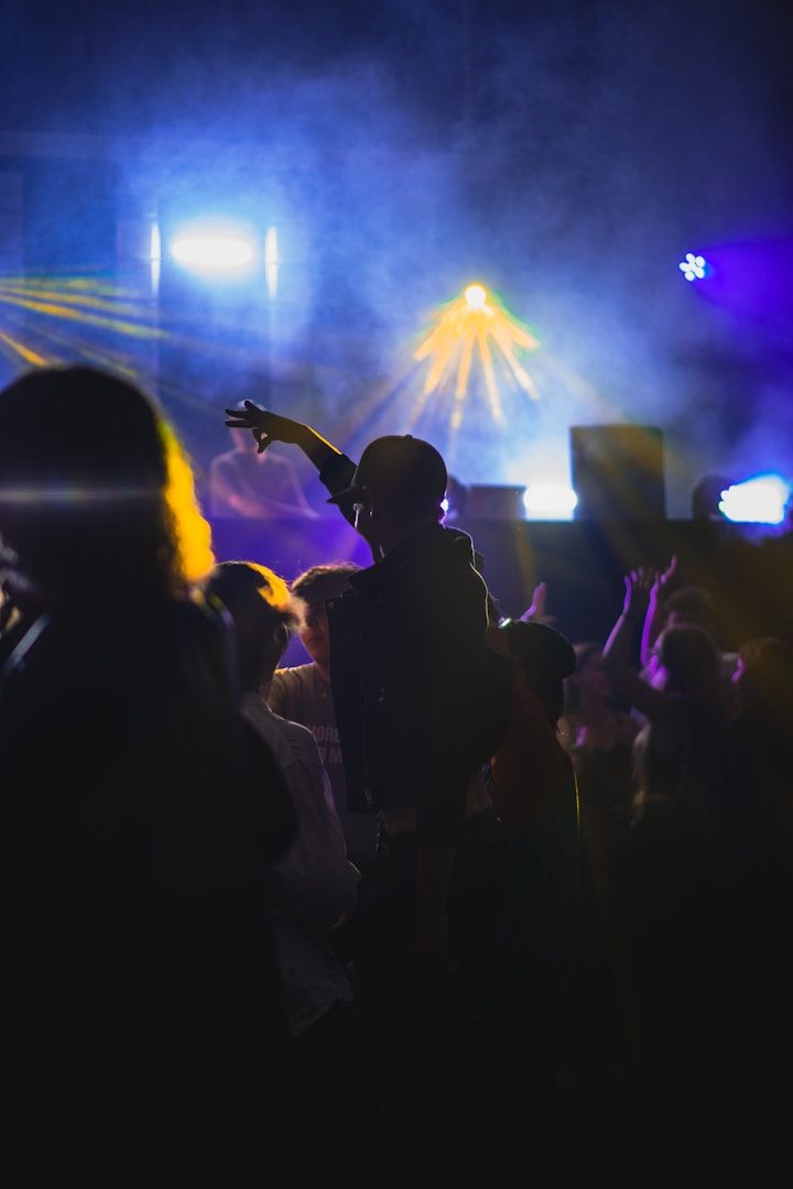 Silhouetted figures dancing at a vibrant, colourful music event with laser lights.